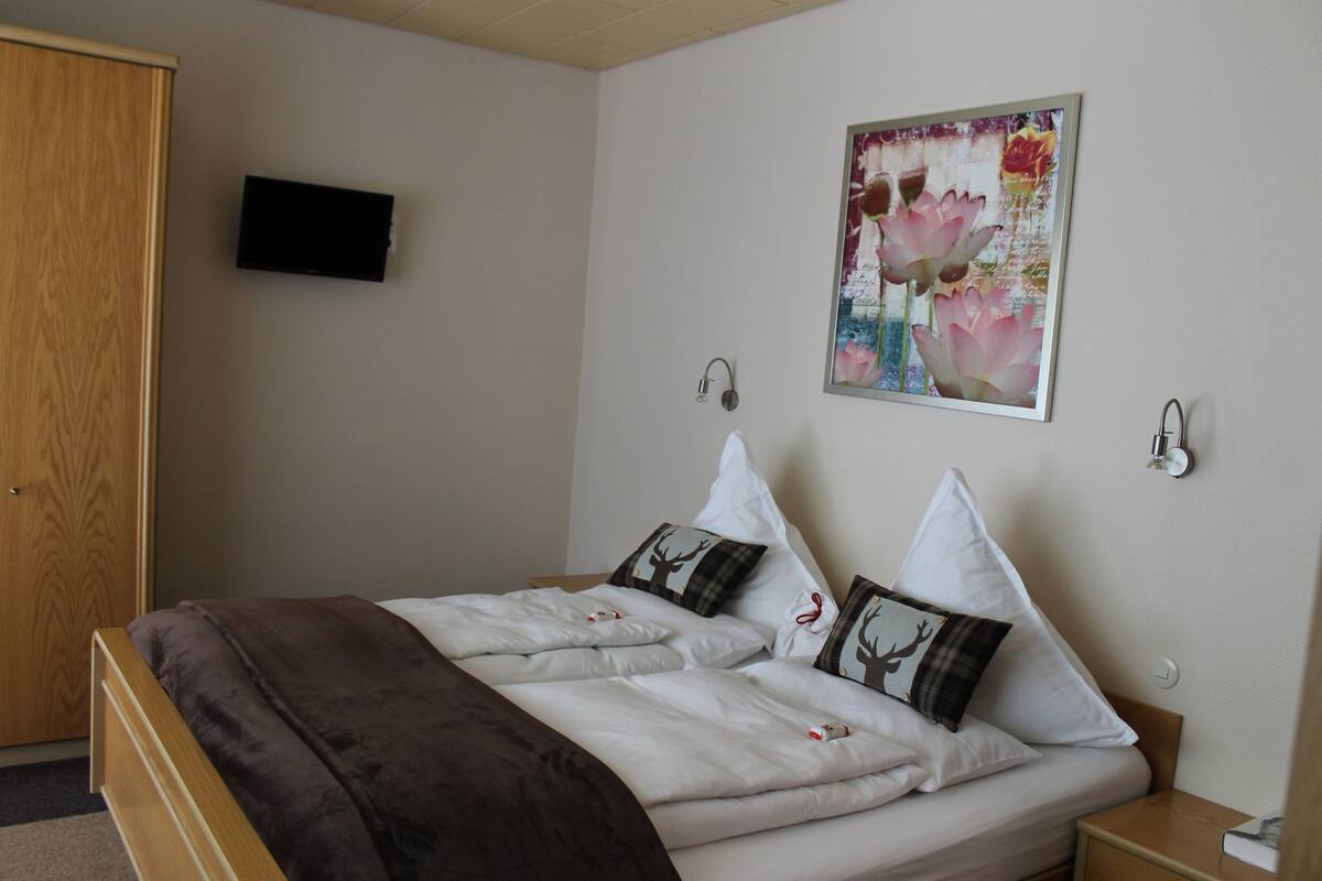 A neatly made bed with a brown blanket, two pillows with reindeer designs, and a wall-mounted painting of flowers.