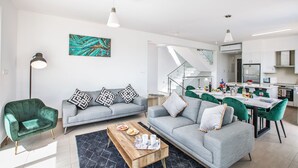 Una sala moderna con un sofá gris, un sillón verde y una zona de comedor con mesa y sillas.