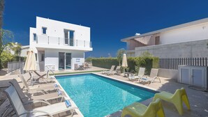 Una casa moderna de dos pisos con piscina, mobiliario exterior y cielo azul despejado.