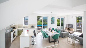 Una cocina moderna con comedor, ventanas amplias y una sala de estar con sofá y televisor.