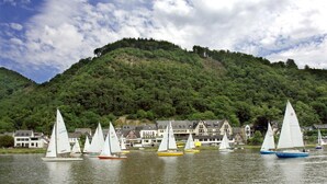 A lakeside village with sailboats, traditional houses, and a forested hill in the background. - Pension Haus am Walde (Brodenbach)