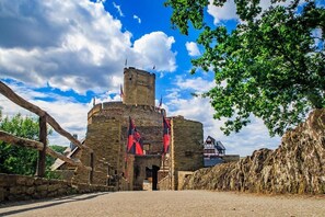 A historic stone building with a tower, flags, and a rustic entrance. - Pension Haus am Walde (Brodenbach)