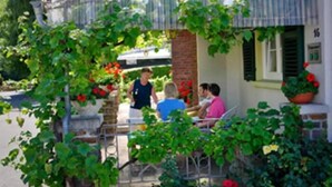 A building with a covered patio area, a brick wall, and a number '15' on the side. - Pension Haus am Walde (Brodenbach)