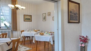 A dining area with tables set for a meal, framed pictures on the wall, and a window with curtains. - Pension Haus am Walde (Brodenbach)