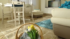 A living room with a white sofa, a dining table with chairs, a TV, and a basket of flowers on the floor.