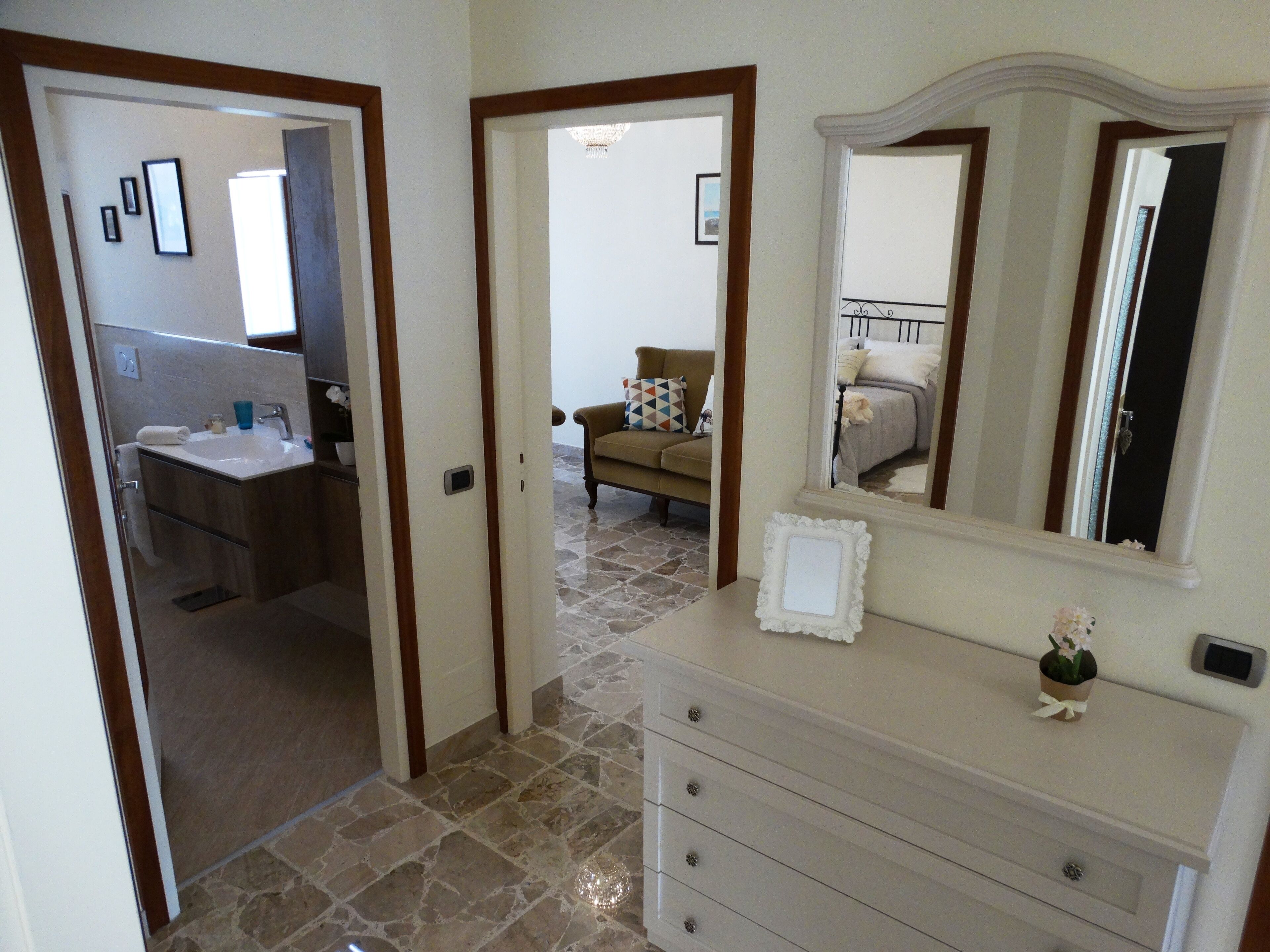 A bathroom with a sink and mirror, a hallway leading to a bedroom, and a dresser with drawers.