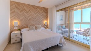 Ein Schlafzimmer mit Bett, Nachttischen, einem Deckenventilator und Blick auf den Strand durch eine Glastür.
