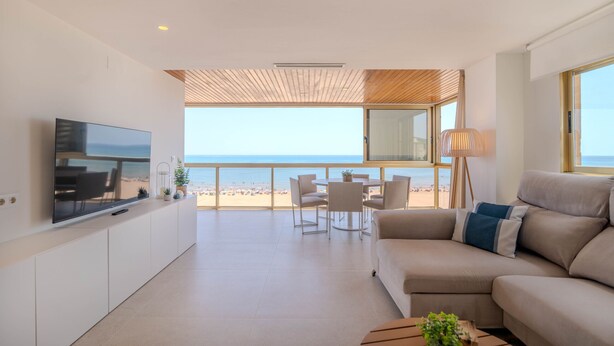 Ein modernes Wohnzimmer mit Fernseher, Sofa und Essbereich mit Blick auf einen Strand.