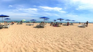 Ein Sandstrand mit Liegestühlen und blauen Sonnenschirmen.
