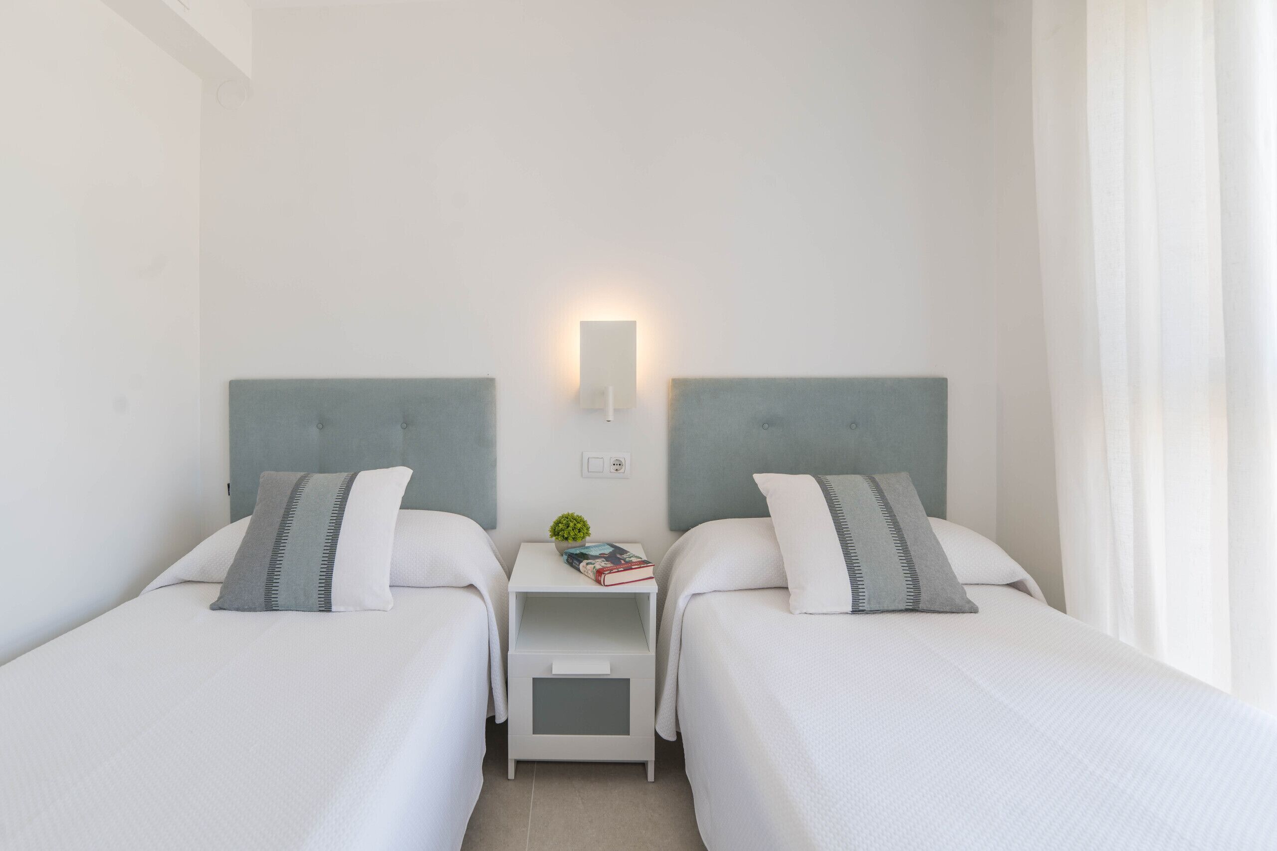 Une chambre d’hôtel avec deux lits, une table de chevet, une lampe fixée au mur et une fenêtre avec des rideaux.