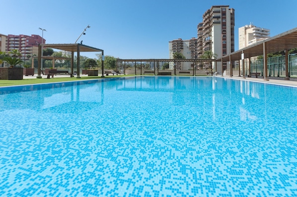 Une piscine dont le fond est recouvert de carrelage, entourée de bancs et agrémentée d’une structure en forme de pergola.