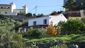 Un quartier résidentiel avec une maison blanche dotée d’un toit recouvert de tuiles rouges, entourée d’une végétation luxuriante et d’un mur de pierre.