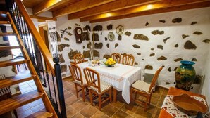 Un coin repas avec un mur en pierre, des chaises en bois, une table recouverte d’une nappe blanche et un vase posé sur la table.