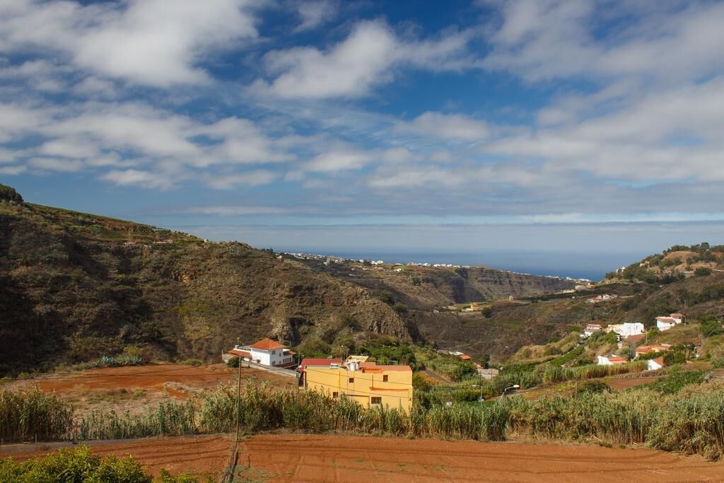 A coastal landscape with a yellow building, terraced fields, and a distant view of the sea.