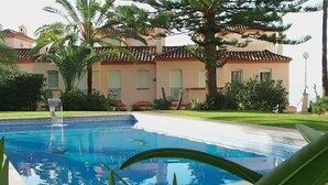 Une piscine bordée de carreaux, entourée de verdure et adossée à un bâtiment dont le toit est également recouvert de carreaux.