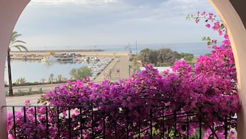 Ein Balkon mit Blick auf einen Hafen und das Meer, umgeben von rosa Bougainvillea-Blüten.