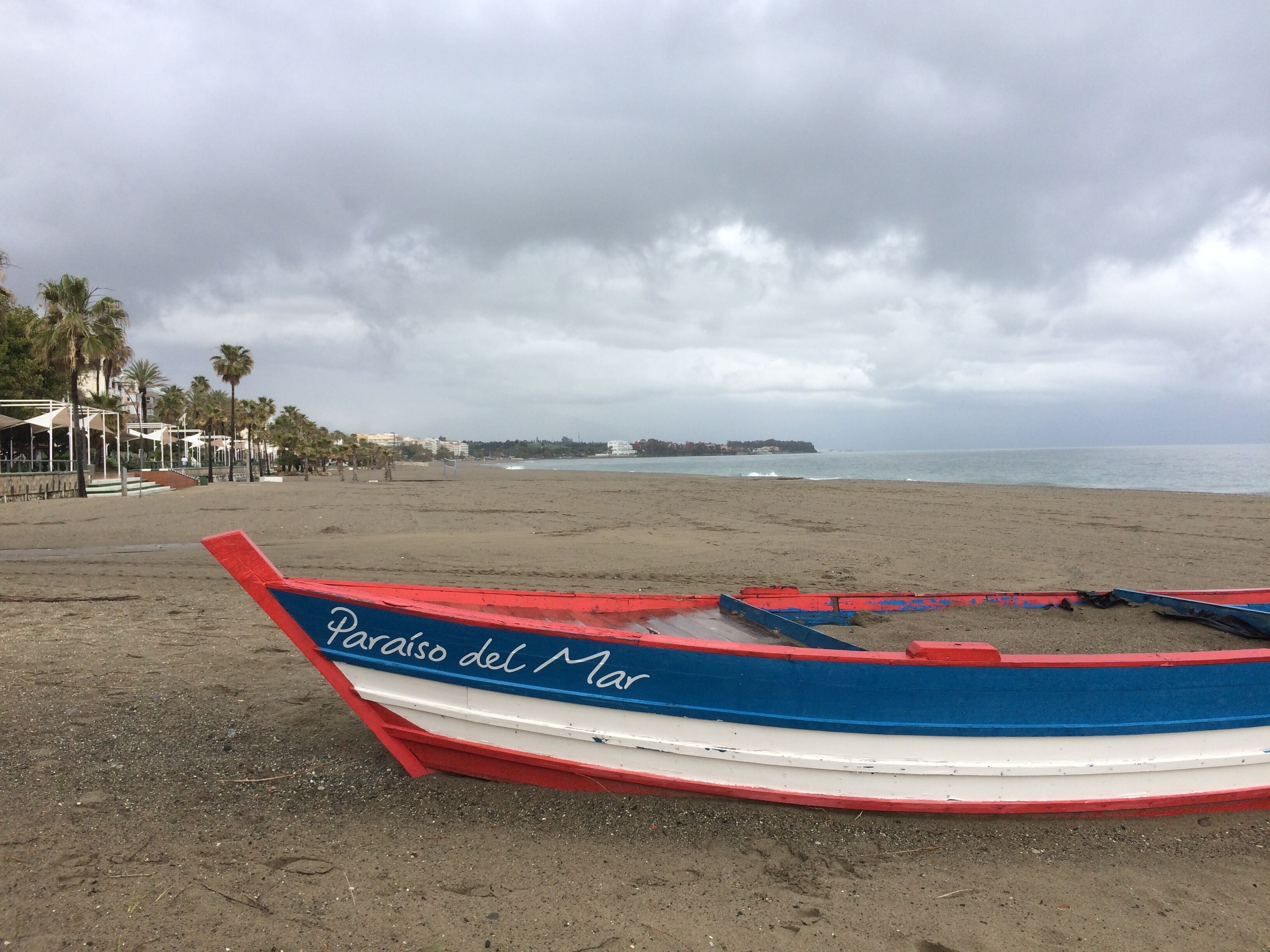 A beach with a row of boats, a sandy shore, and a cloudy sky.