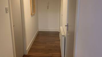 A hallway with wooden flooring, white walls, and a ceiling light fixture.