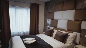 Una habitación de hotel moderna con una cama grande, un cabecero de diseño geométrico y una ventana con cortinas.