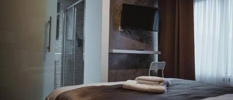 Habitación de hotel moderna con una cama grande, un televisor montado y una zona de ducha visible a través de una puerta abierta.