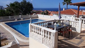 A rooftop pool area with a view of the sea, outdoor seating, and a pergola.