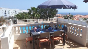 An outdoor dining area with a table and chairs, an umbrella, and a view of the sea.