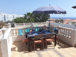 Un espace de restauration en plein air avec une table et des chaises, un parasol et une vue sur la mer.