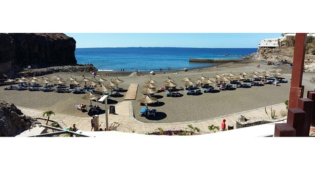 A beach with rows of sun loungers and thatched umbrellas, a wooden walkway, and a view of the sea.