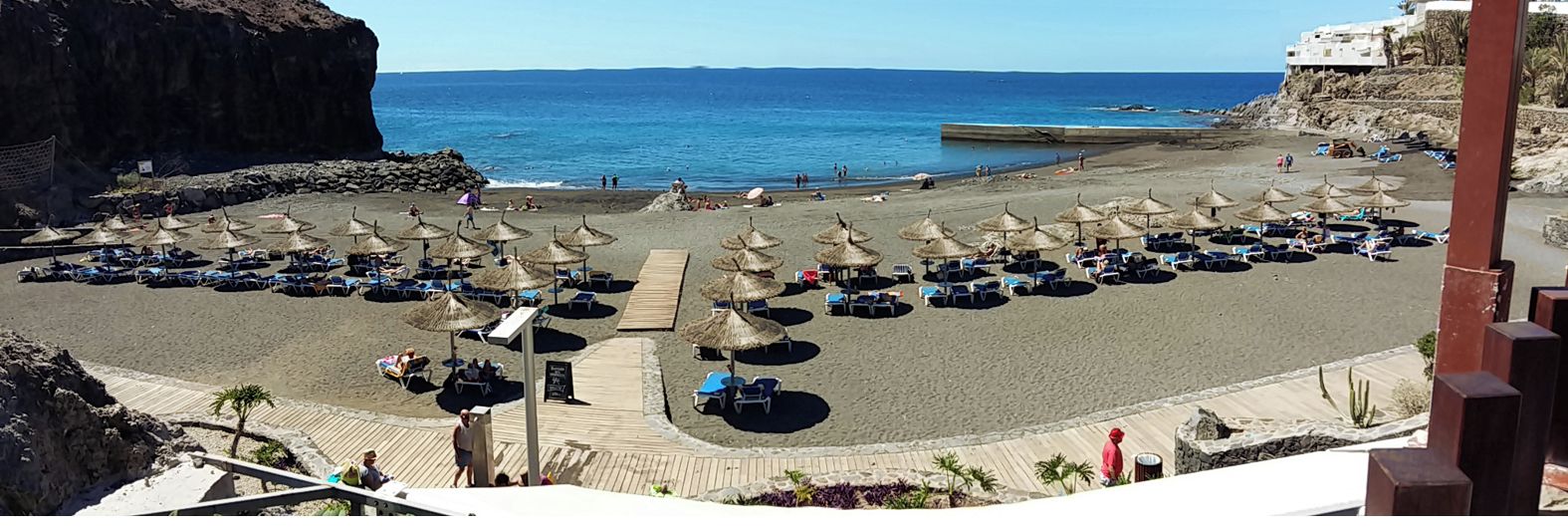 Une plage bordée de rangées de chaises longues et d’ombrelles en chaume, une promenade en bois et une vue sur la mer.