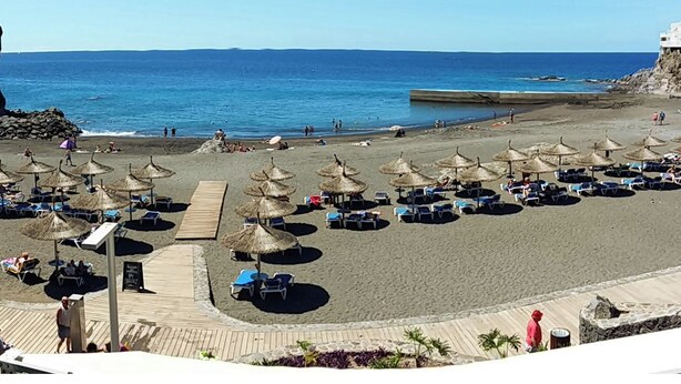 Une plage bordée de rangées de chaises longues et d’ombrelles en chaume, une promenade en bois et une vue sur la mer.