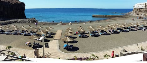 Une plage bordée de rangées de chaises longues et d’ombrelles en chaume, une promenade en bois et une vue sur la mer.
