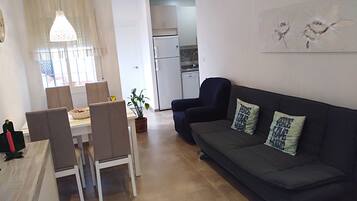 Un salon moderne avec un canapé, des fauteuils, une table à manger et une cuisine en arrière-plan.