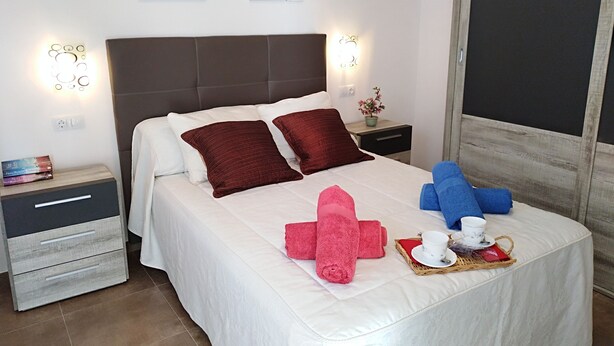 A neatly made bed with white and red bedding, a bedside table with a lamp, and a wall-mounted artwork. - Beautiful and sunny house in Cordoba (Córdoba)