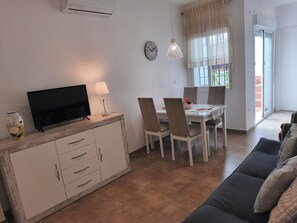 Een moderne woonkamer met een flatscreen televisie, een eettafel met stoelen, een bank en een decoratieve vaas.