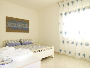 A bedroom with a bed, a nightstand, a bedside table, and a window with a curtain.