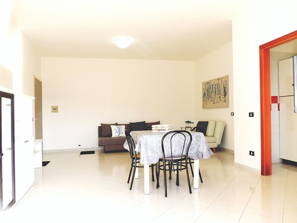 A dining area with a table and chairs, a sofa, and a painting on the wall.