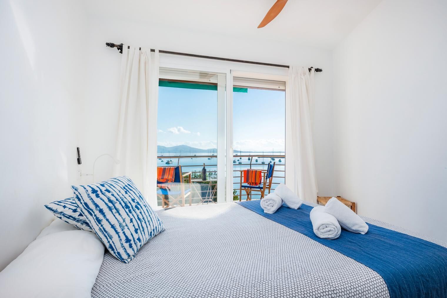 Un dormitorio con cama, vista al mar y balcón con sillas.