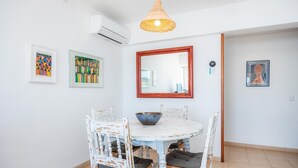 A dining area with a round table, white chairs, a bowl, a mirror, and two framed artworks on the walls. - Two bedroom air conditioned apartment on the Pine Walk. Amazing Sea Views. WIFI (Pollença)
