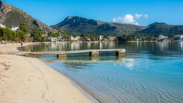 A beach with clear water, a concrete pier, and a mountainous backdrop. - Two bedroom air conditioned apartment on the Pine Walk. Amazing Sea Views. WIFI (Pollença)