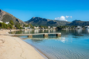 A beach with clear water, a concrete pier, and a mountainous backdrop.