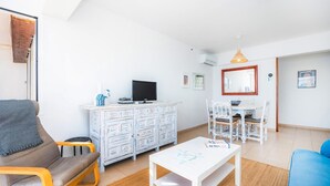 A modern living room with a sofa, a white coffee table, a TV on a white cabinet, and a dining area with a table and chairs. - Two bedroom air conditioned apartment on the Pine Walk. Amazing Sea Views. WIFI (Pollença)