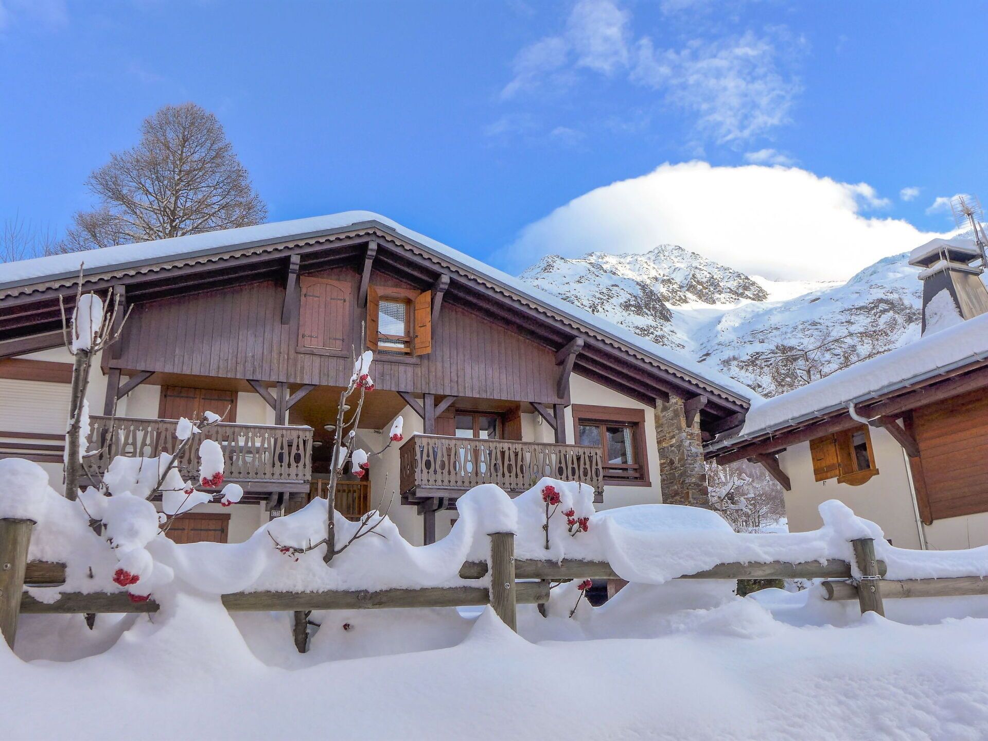 A wooden chalet with a balcony, surrounded by snow-covered trees and mountains.