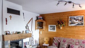 Een gezellige woonkamer met een stenen openhaard, houten wanden, een bank met gestreepte kussens, een houten bijzettafeltje en een ingelijst schilderij aan de muur.
