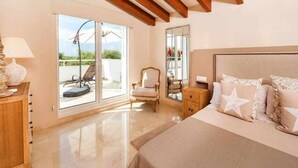 Een slaapkamer met een groot bed, een stoel, een nachtkastje en een schuifdeur die uitkomt op een buitenruimte.