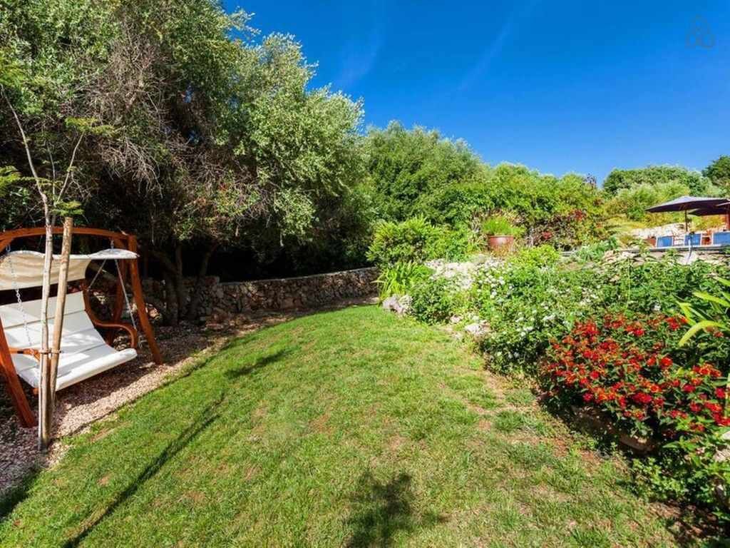 A well-maintained garden with a swing set, a stone wall, and a variety of plants and flowers.