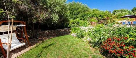 A well-maintained garden with a swing set, a stone wall, and a variety of plants and flowers.