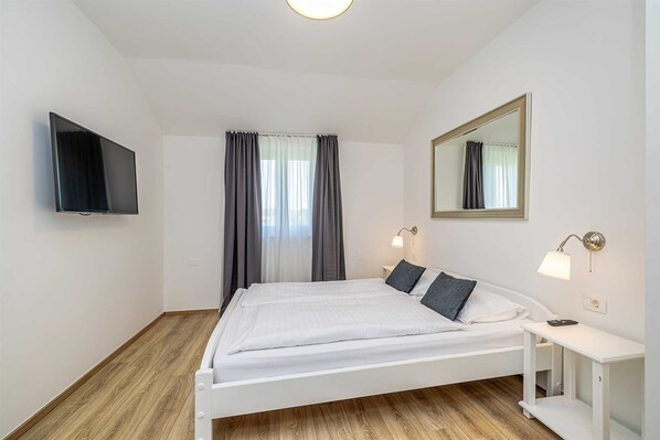 Une chambre à coucher avec un lit, un téléviseur fixé au mur, une table de chevet avec une lampe et un miroir.