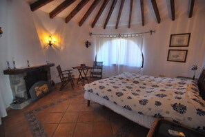 A bedroom with a bed, a fireplace, a window with curtains, a small table, and a chair. - Wonderful holiday villa with private pool, air condition (Xàbia)