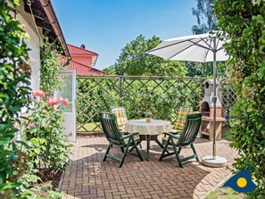 An outdoor patio with a table and chairs, a brick floor, a wooden fence, and a brick oven. - Eichelhäher Vacation Home - A Retreat with a Grill & Terrace - Eichelhäher (Heringsdorf)