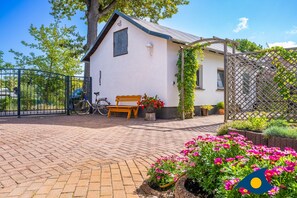Un bâtiment blanc avec un toit en pente, un banc en bois et un vélo garé à l’extérieur.